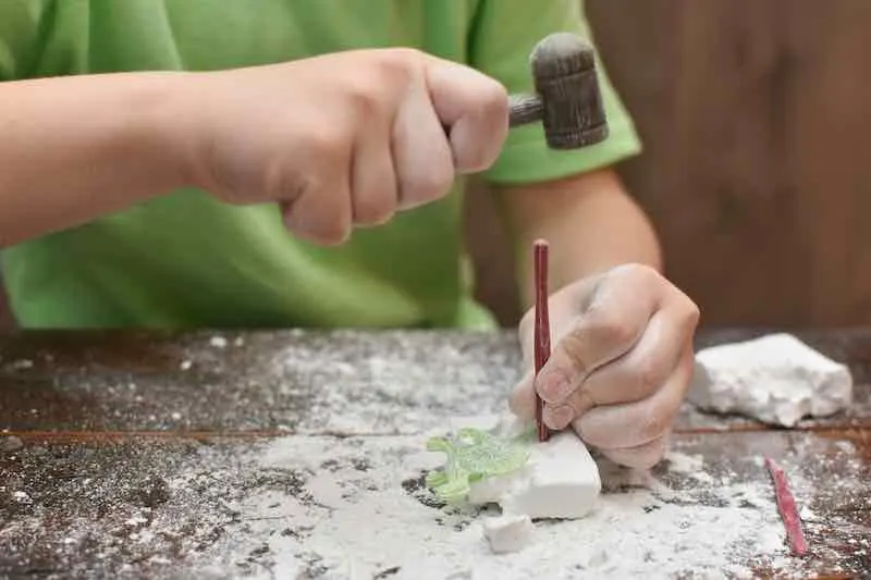 Child's hand is playing with the archaeological set. Child digging a dinosaur.