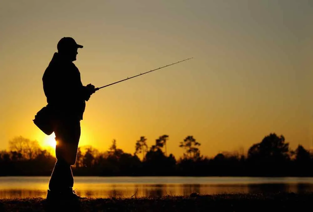 A fisherman silhouette fishing at sunset. Perhaps he's fishing at  Clear Lake State Park Michigan.