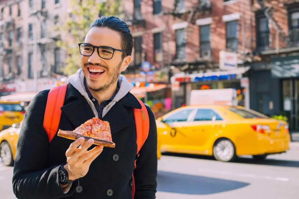 man on street eating pizza in New York