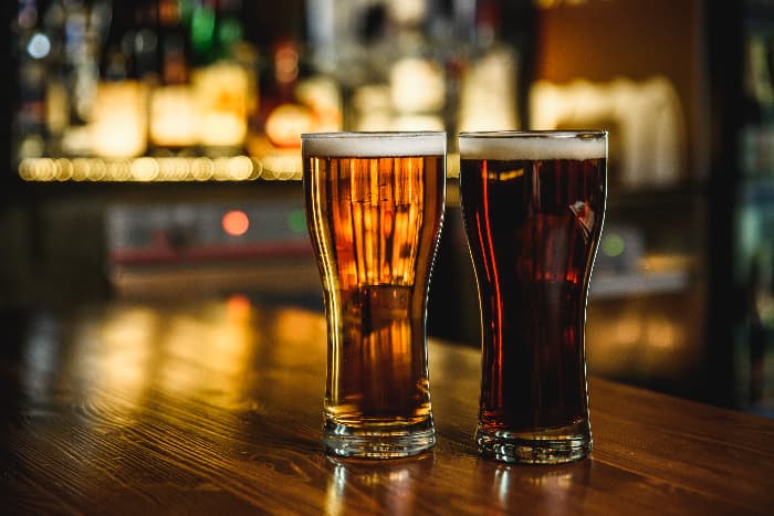 Two glasses of beer, one light and one dark, in pub or bar setting.