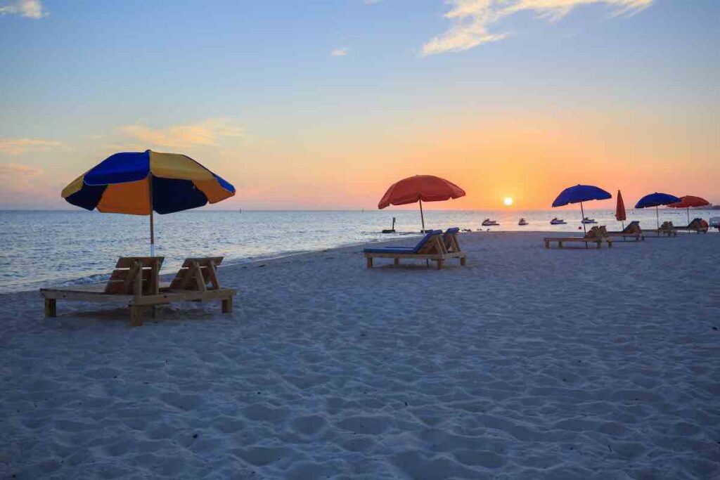 Sunset at a beach with chaise loungers and umbrellas.