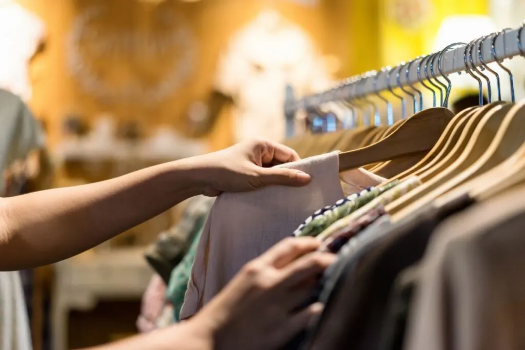 Hand shifting through clothes on a clothing rack. Perhaps at one of the best thrift stores in Michigan.