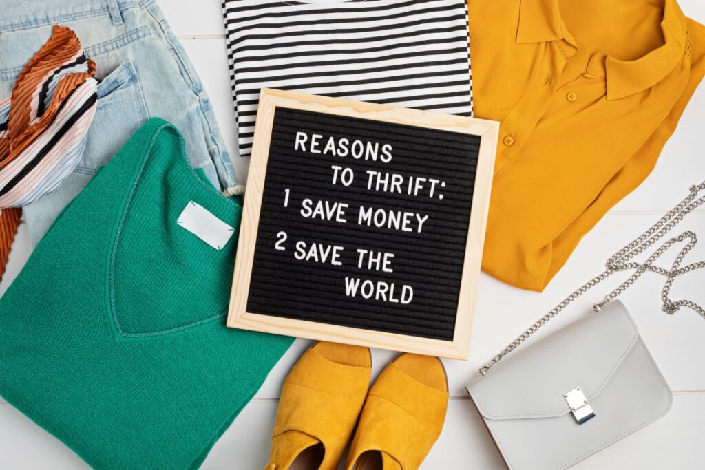 An assortment of thrifted clothing and a sign that gives reasons to thrift shop. 