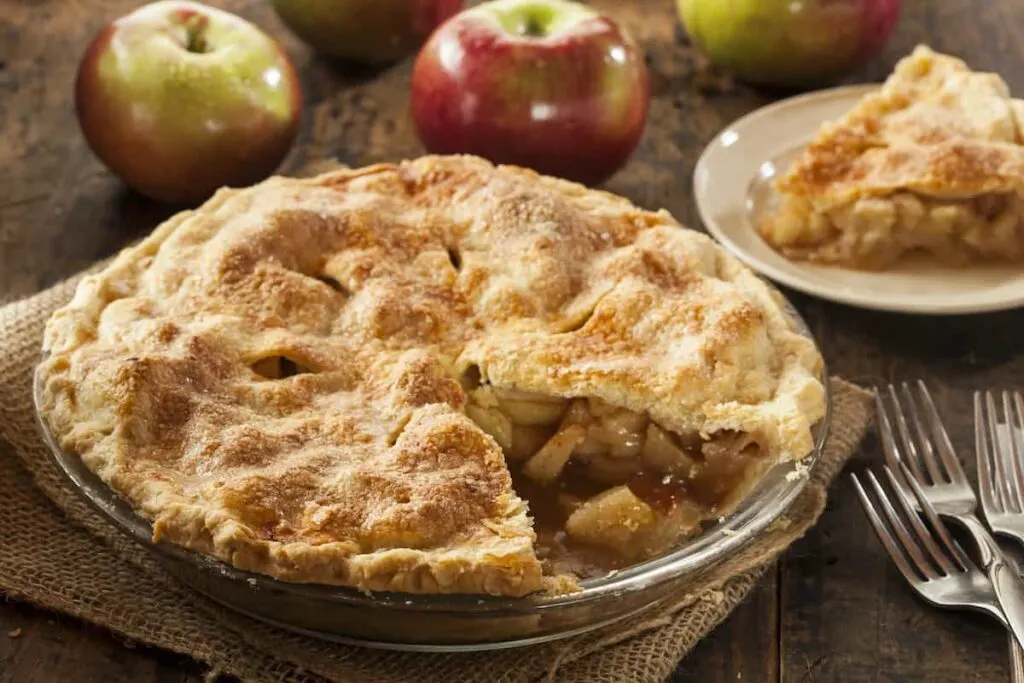 An apple pie with a plated wedge in the background.