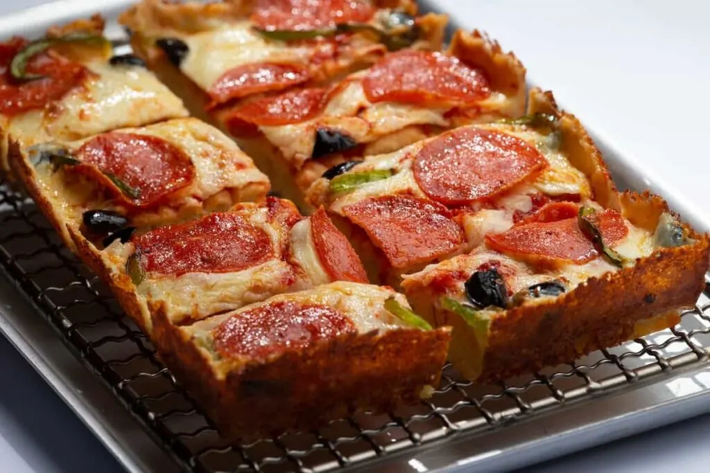 A square Detroit-style pizza loaded with cheese, pepperoni, green peppers, and olives.